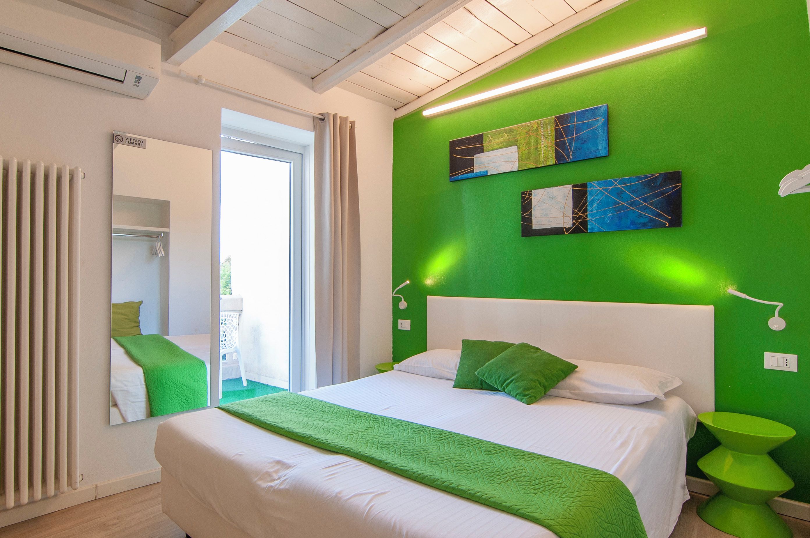 Una camera d'albergo con un letto, una parete verde e uno specchio.