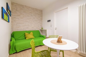 Een kamer met een groene bank, een witte ronde tafel en groene stoelen.