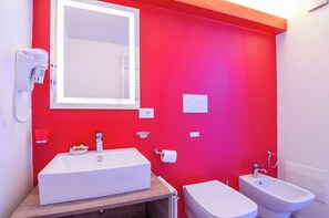 A bathroom with a red wall, a white sink, a bidet, a mirror, and a hairdryer. - Kedimore - Red Apartment (Verona)