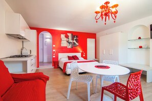 A modern hotel room with a red and white color scheme, a dining area with a round table, and a kitchen with a stove. - Kedimore - Red Apartment (Verona)