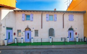 A building with a green lawn, a blue door, and a sign with a cartoon character. - Kedimore - Red Apartment (Verona)