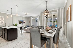 A modern kitchen with a central island, dining area with grey upholstered chairs, and a large window with curtains. - Magical Getaway With Private Pool, Top Location (Davenport)