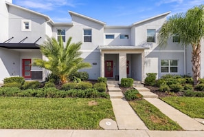 A modern two-story residential building with a red door, a covered porch, and a well-maintained front yard with grass and shrubs. - Magical Getaway With Private Pool, Top Location (Davenport)
