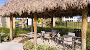 An outdoor patio with thatched roof seating and tables, surrounded by greenery and a view of a residential area. - Magical Getaway With Private Pool, Top Location (Davenport)