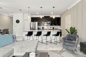 A modern kitchen with dark cabinets, a stainless steel refrigerator, and a microwave. There are three pendant lights hanging above the island. - Magical Getaway With Private Pool, Top Location (Davenport)