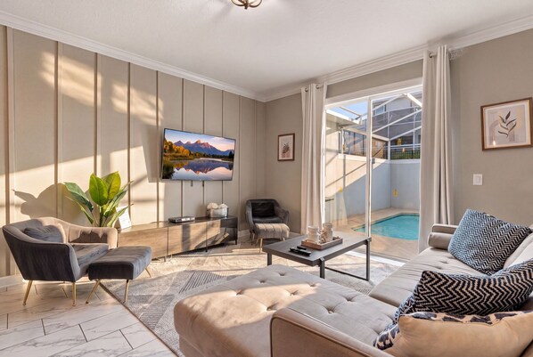 A modern living room with a flat-screen TV, comfortable seating, a coffee table, and a view of a swimming pool. - Magical Getaway With Private Pool, Top Location (Davenport)