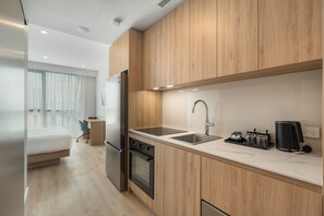 A modern kitchen with wooden cabinets, a stainless steel refrigerator, a built-in oven, a sink, and a coffee maker.