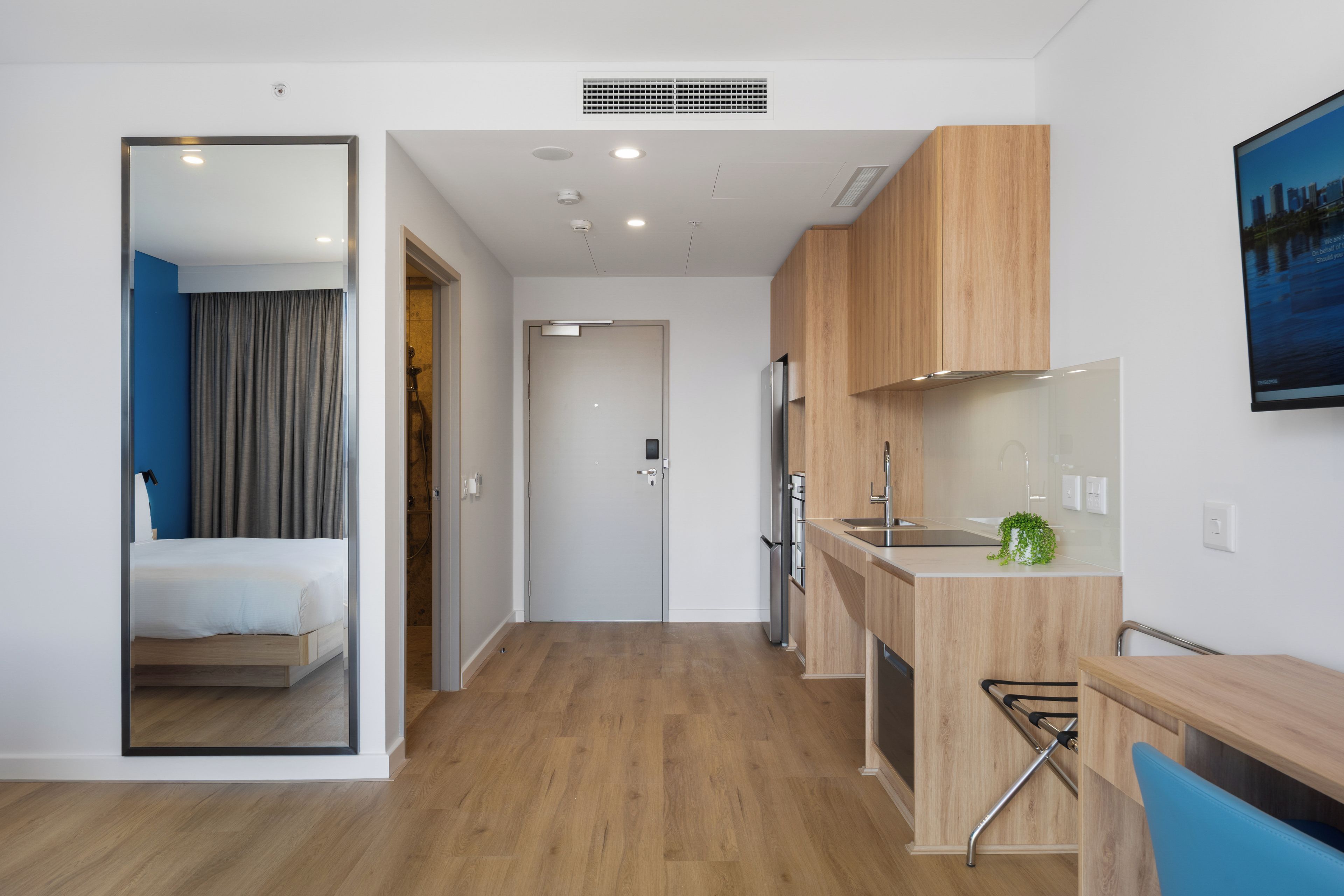 A modern hotel room with a bed, a bathroom, a kitchenette, and a small seating area.