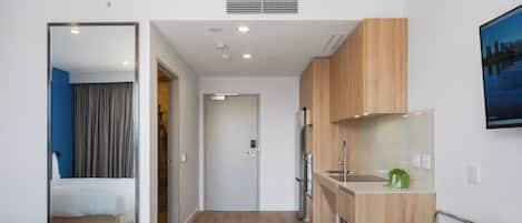 A modern hotel room with a bed, a bathroom, a kitchenette, and a small seating area.