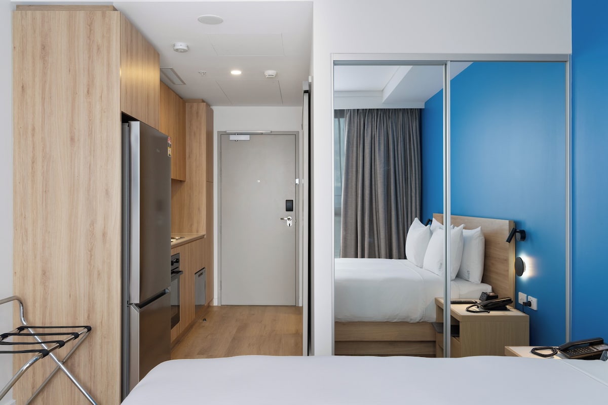 A hotel room with a bed, bedside table, and a view through a glass door.