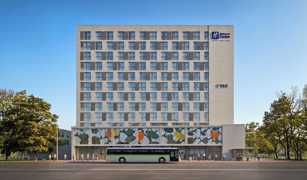 A multi-story building with a Holiday Inn Express logo, a bus in front, and a large windowed facade.