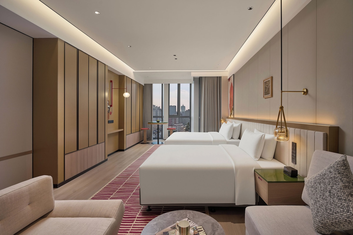 Habitació d'hotel amb dos llits, zona de seients, vista a la ciutat i minibar.