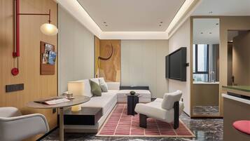 Une chambre d’hôtel moderne, dotée d’un canapé, de fauteuils, d’une petite table, d’un téléviseur et offrant une vue sur la ville.