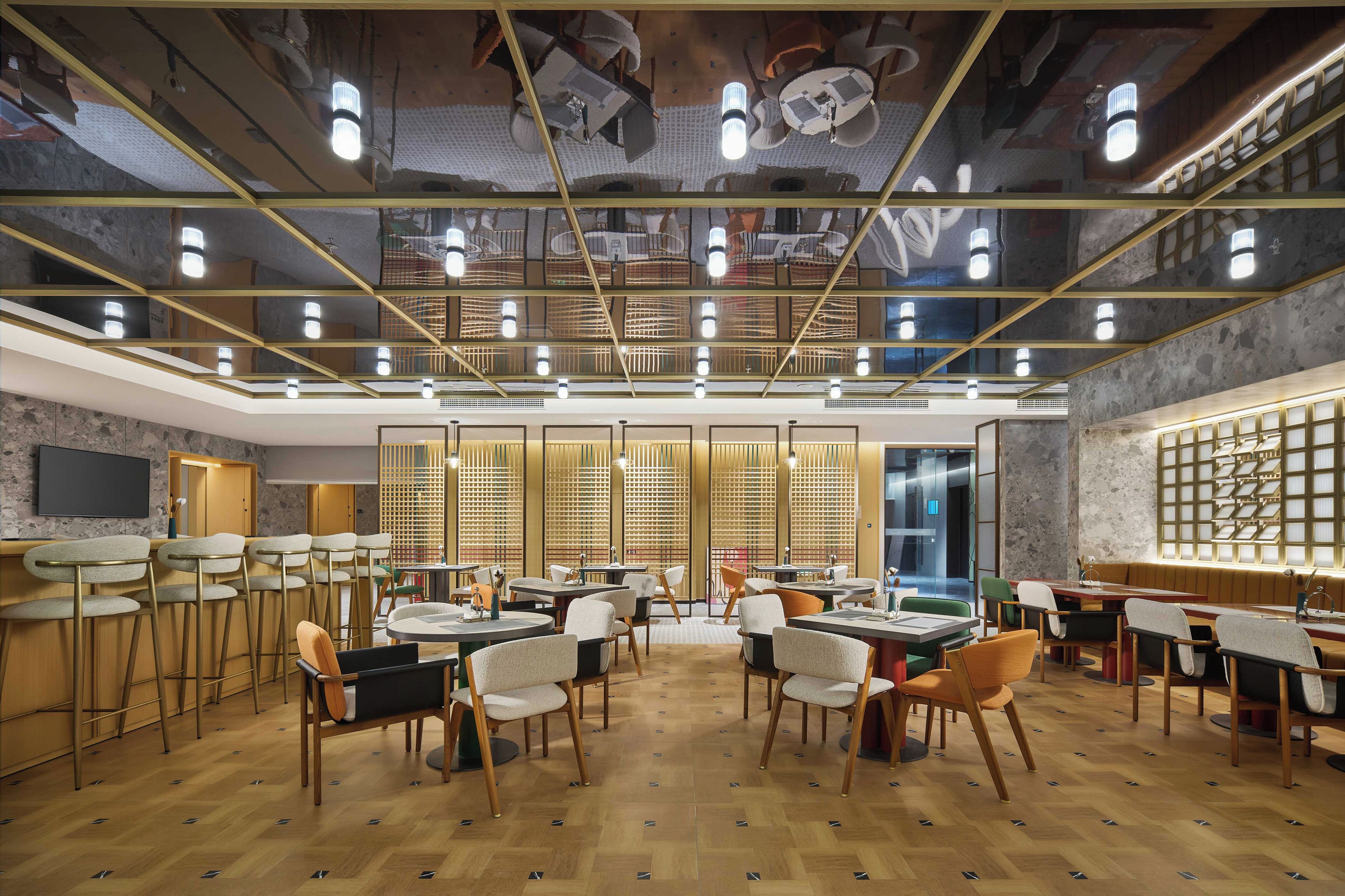 Un intérieur moderne doté de plusieurs espaces de détente, notamment des tabourets de bar et des tables, ainsi qu’un grand écran mural.