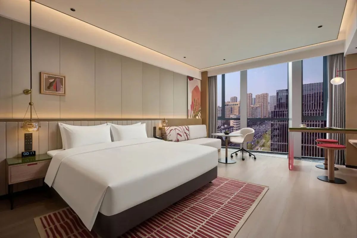 Habitació d'hotel moderna amb un llit gran, una taula de treball, una cadira i vistes a la ciutat.