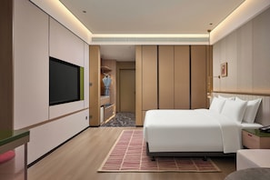 Una habitació d'hotel moderna amb un llit gran, televisió de pantalla plana, un armari i una petita zona de treball.