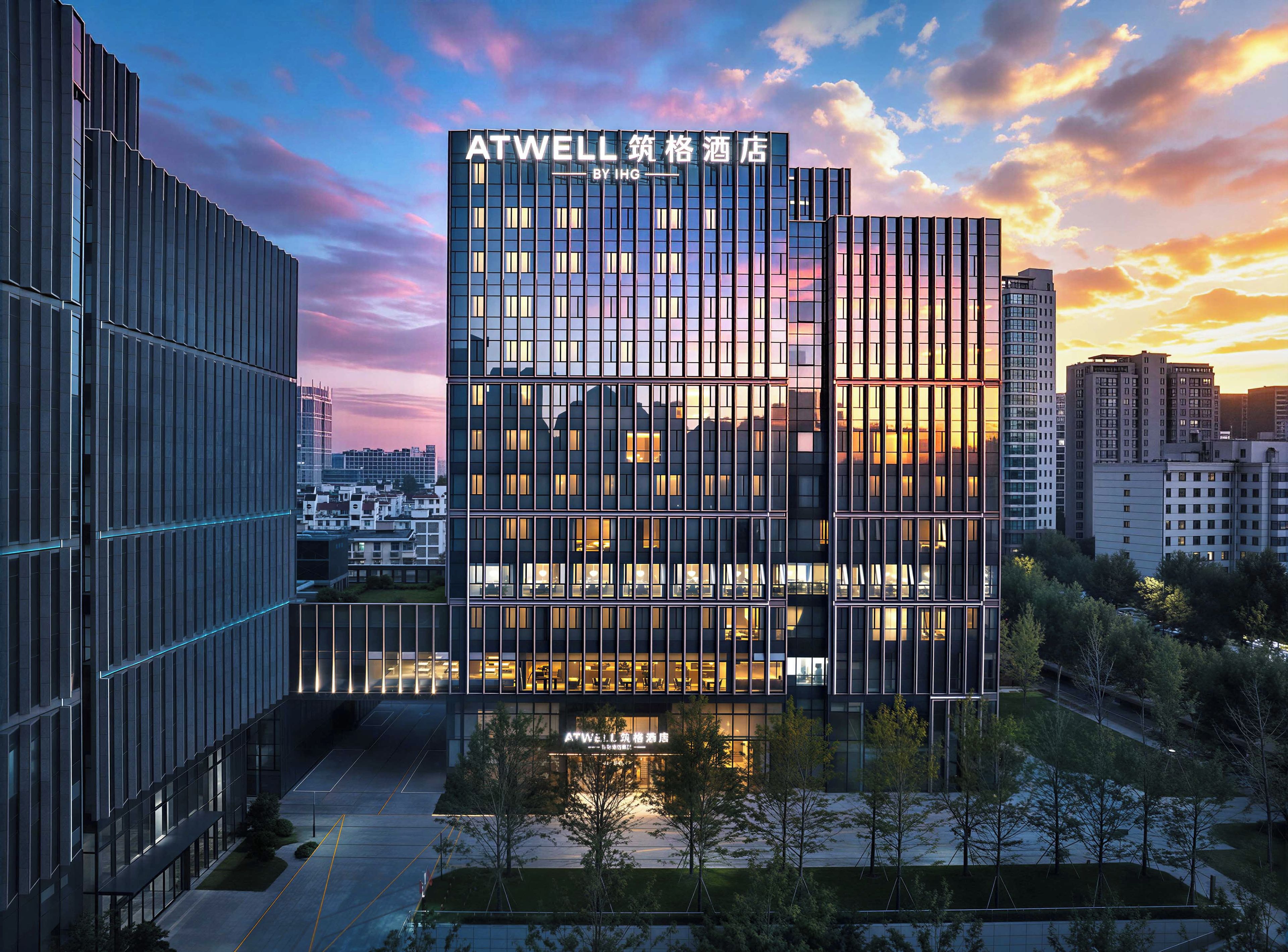 Un hôtel moderne, reconnaissable à son grand panneau ATWELL, entouré d’autres bâtiments et situé sous un ciel dégagé.