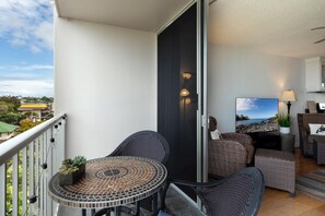 A balcony with a round table and chairs, a sliding door, and a television on the right. - Kailua Village#609 High Floor, Heart of Downtown! (Kailua-Kona)