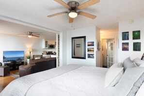 A bedroom with a large bed, a ceiling fan, and a view into the kitchen area. - Kailua Village#609 High Floor, Heart of Downtown! (Kailua-Kona)