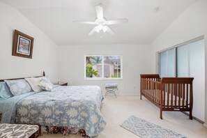 Une chambre à coucher avec un lit, un berceau, une fenêtre et un ventilateur de plafond.