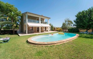 Casa de dos pisos con piscina y zona de estar exterior.