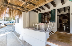 A covered outdoor seating area with a table and chairs, a thatched roof, and a view of the street. - Nice home in pollença with house sea view (POLLENÇA)