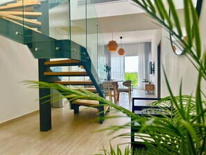 Un interior moderno con una escalera de cristal, suelo de madera, una zona de comedor y lámparas colgantes.