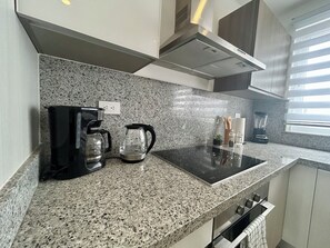 Eine Küche mit Granit Arbeitsplatten, einer Kaffeemaschine, einem Wasserkocher, einem Mixer und einem Fenster mit Jalousien.