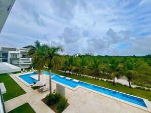 Ein modernes Hotel mit Schwimmbad, Palmen und Blick auf eine Stadtlandschaft.