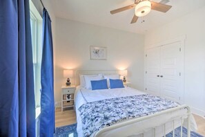 A bedroom with a bed, bedside lamps, a ceiling fan, a door, and a window with curtains. - Canyon Lake Cottage w Deck, Grill & Fast WiFi! (Canyon Lake)