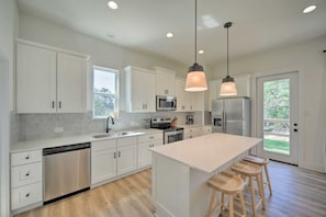 A modern kitchen with white cabinetry, stainless steel appliances, and a central island with bar stools. - Canyon Lake Cottage w Deck, Grill & Fast WiFi! (Canyon Lake)