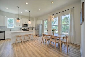 Une cuisine moderne avec des meubles blancs, un îlot central doté de tabourets, un réfrigérateur en acier inoxydable et des luminaires suspendus.