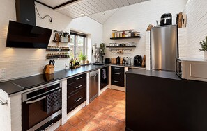 A modern kitchen with a black countertop, stainless steel appliances, and a white brick wall. - Cozy home in Broager with WiFi (Broager)