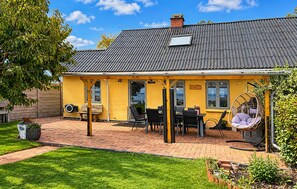 A yellow building with a tiled roof, a patio area with chairs and a table, and a hanging chair. - Cozy home in Broager with WiFi (Broager)