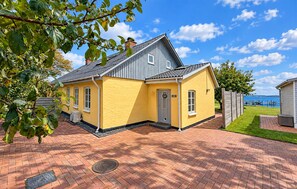 A yellow house with a grey roof, a brick driveway, and a view of the water. - Cozy home in Broager with WiFi (Broager)