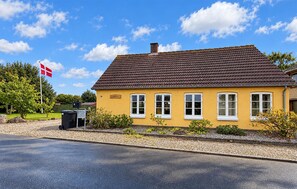 Ein gelbes Gebäude mit einem braunen Dach, einer Flagge und einem wolkenlosen Himmel.