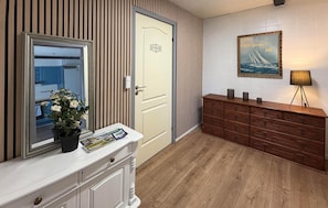 Ein Flur mit einer weißen Tür, auf der 'BADEZIMMER' steht, einem Holzkabinent mit Schubladen, einem Spiegel und einem gerahmten Bild an der Wand.