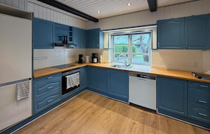 A kitchen with blue cabinets, a wooden countertop, a built-in oven, and a window with a view of greenery. - 3 bedroom beautiful home in Broager (Broager)