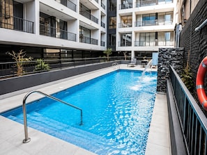 A swimming pool with a water feature, surrounded by a modern building with balconies. - Cozy Apartment in fantastic Santiago near to Movistar Arena and Club Hipico (santiago)