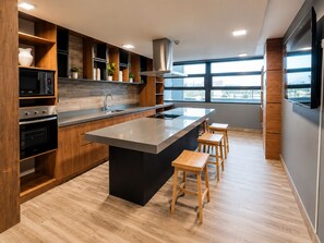 A modern kitchen with wooden cabinetry, a central island, bar stools, and a large window providing natural light. - Cozy Apartment in fantastic Santiago near to Movistar Arena and Club Hipico (santiago)