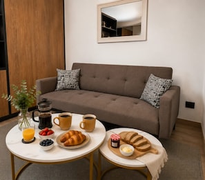 A cozy living area with a sofa, coffee table, and breakfast setup including croissants, bread, and beverages. - Cozy Apartment in fantastic Santiago near to Movistar Arena and Club Hipico (santiago)
