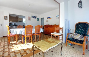 Un comedor con piso a cuadros, sillas de madera, una mesa con mantel estampado y una cocina al fondo.