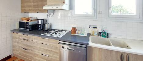 Une cuisine moderne équipée d’une cuisinière à gaz, d’un four à micro-ondes et d’un lave-vaisselle. On y trouve des placards avec des portes en bois et une fenêtre au-dessus de l’évier.