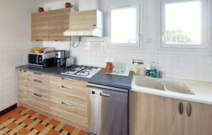 A modern kitchen with a gas stove, microwave, and dishwasher. There are cabinets with wooden doors and a window above the sink. - 3 bedroom beautiful home in Lamballe Armor (Lamballe Armor)