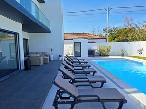 A modern outdoor pool area with lounge chairs, a dining area, and a view of a residential building. - LJR Accommodations São Vicente Ferreira (Ponta Delgada)