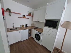 A compact kitchen with white cabinetry, a built-in washing machine, a microwave, and a small sink. - LJR Accommodations São Vicente Ferreira (Ponta Delgada)