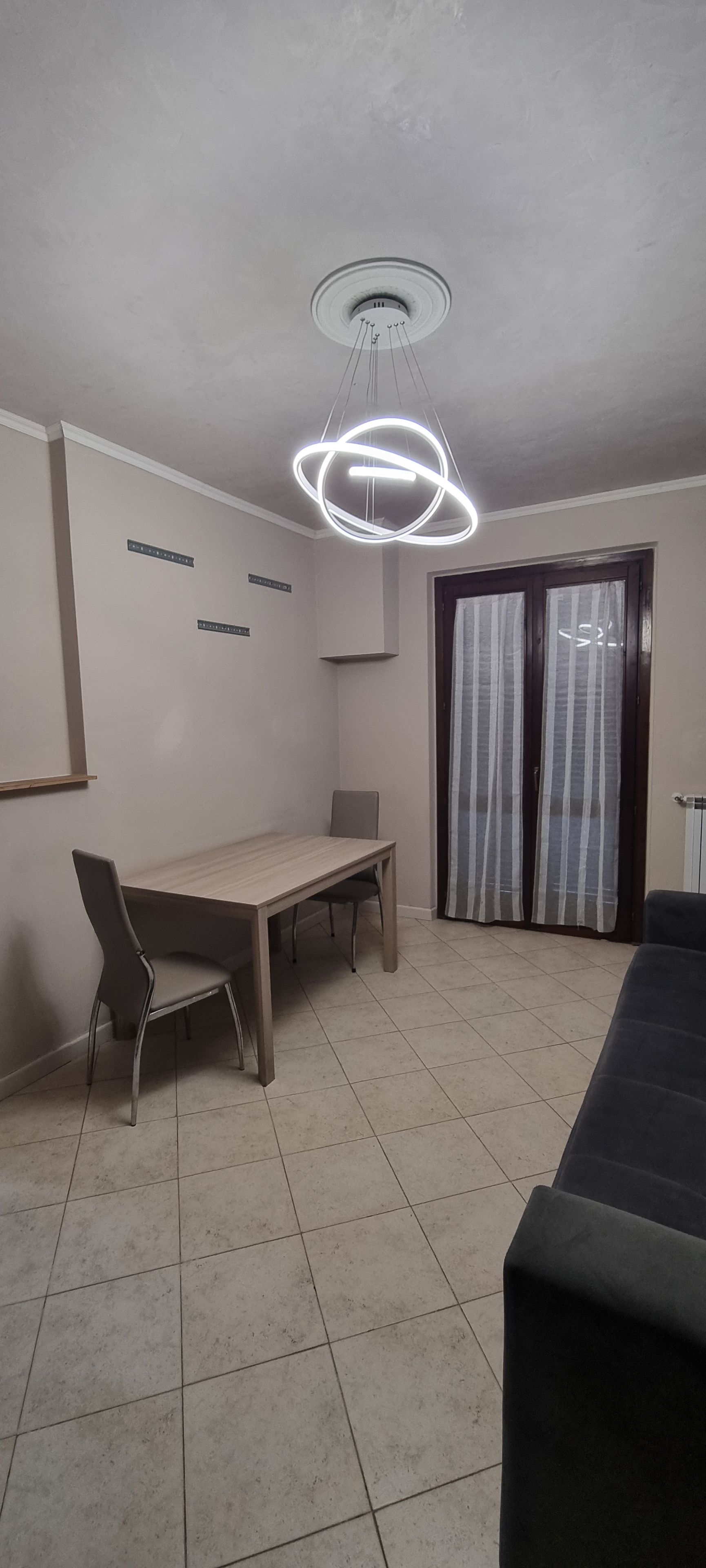 A dining area with a table and chairs, a modern ceiling light fixture, and a sliding glass door with curtains.