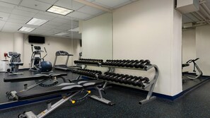 Ein Fitnessraum mit Trainingsgeräten, darunter Laufbänder, ein Ergometer und eine Langhantelbank.