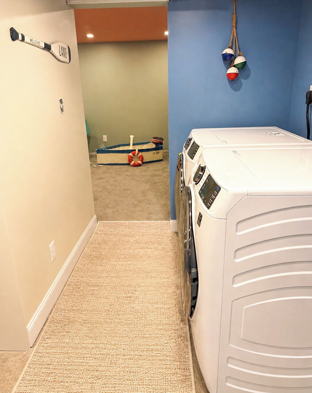 A laundry room with a washing machine and dryer, a welcome sign, and a life preserver on the floor.