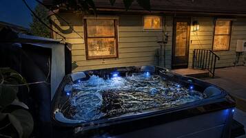 A hot tub in front of a house with a porch and a window.